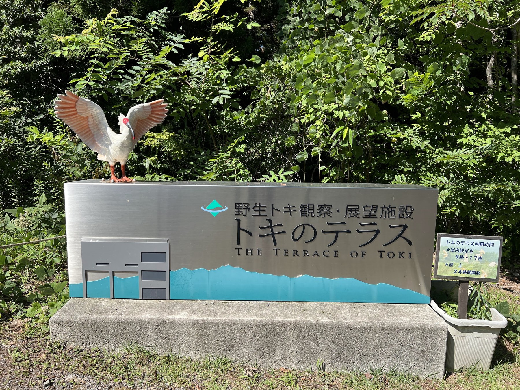 トキのテラスの施設名が書かれた看板。上に翼を広げたトキの像が置かれている。